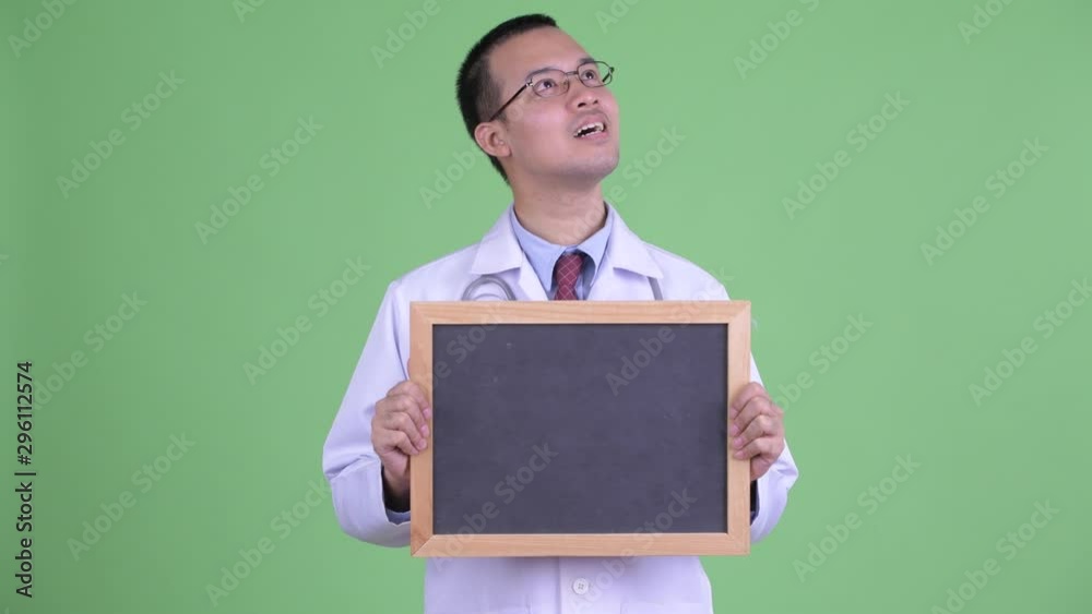 Happy Asian man doctor thinking while holding blackboard Happy Asian man doctor thinking while holding blackboard