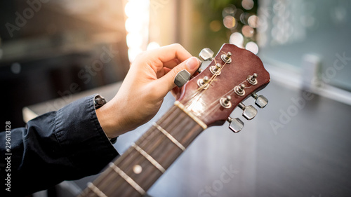 Male hand guitarist adjusting pegs on acoustic guitar during music lesson at home. String musical instrument concept