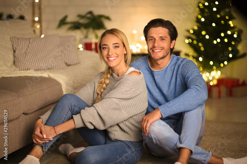 Happy millennial couple sitting in front of Christmas tree