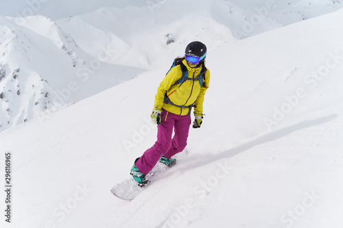 Woman in helmet and mask is riding on snowboard on snowy slope at winter day.