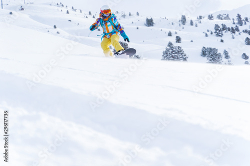 Sports woman in helmet and mask is riding on snowboard on snowy slope at winter day.
