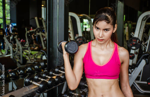 Young beautiful woman doing exercises lifting dumbbell in gym.Glad girl is enjoying with her training process in the morning. She is working hard