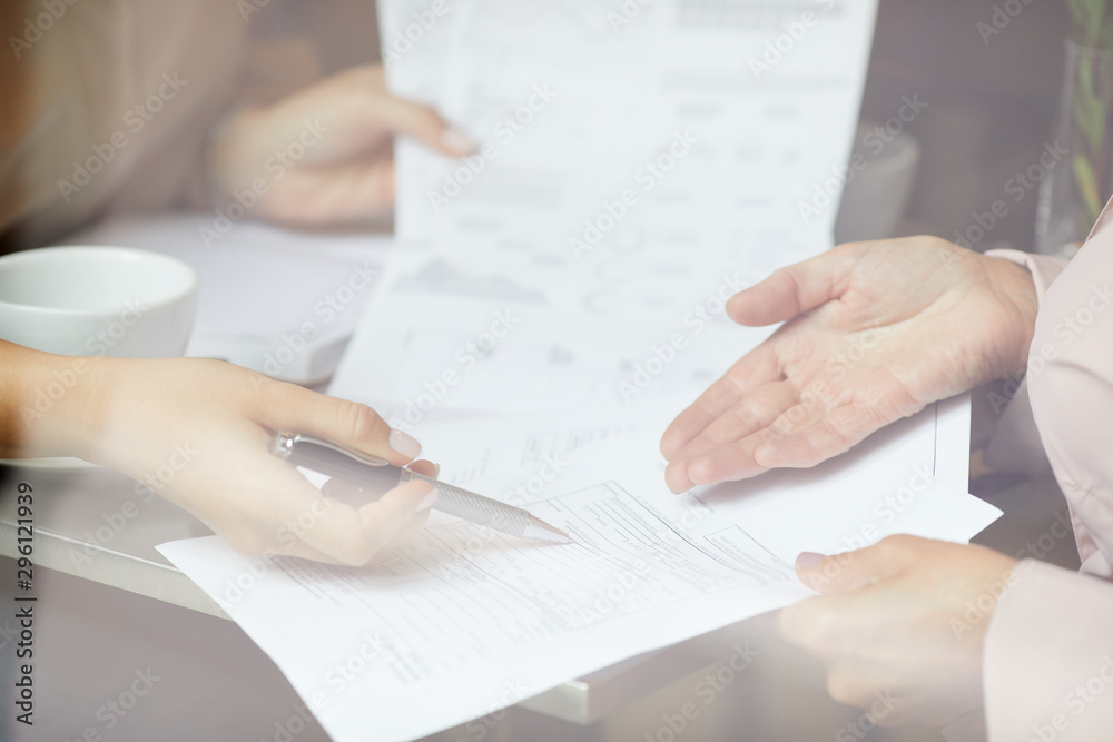 Close-up of businesswomen sitting at the table and discussing business contract during business meeting Close-up of businesswomen sitting at the table and discussing business contract during business meeting