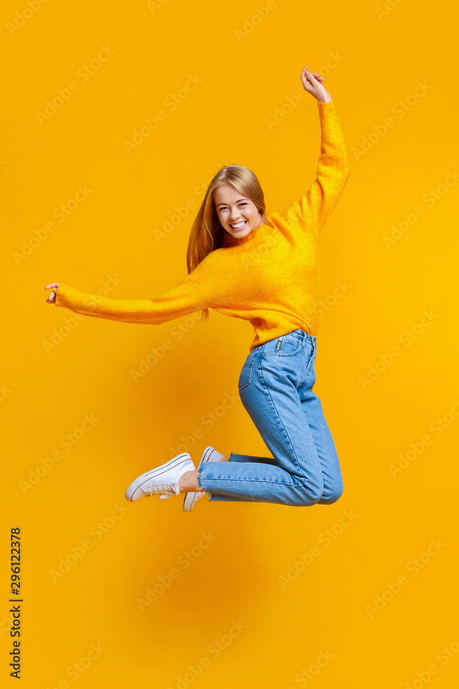 Joyful teen girl jumping in air on orange background - obrazy, fototapety, plakaty 
