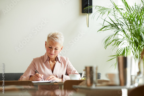 Serious mature businesswoman concentrating on her work she making notes at the table at office