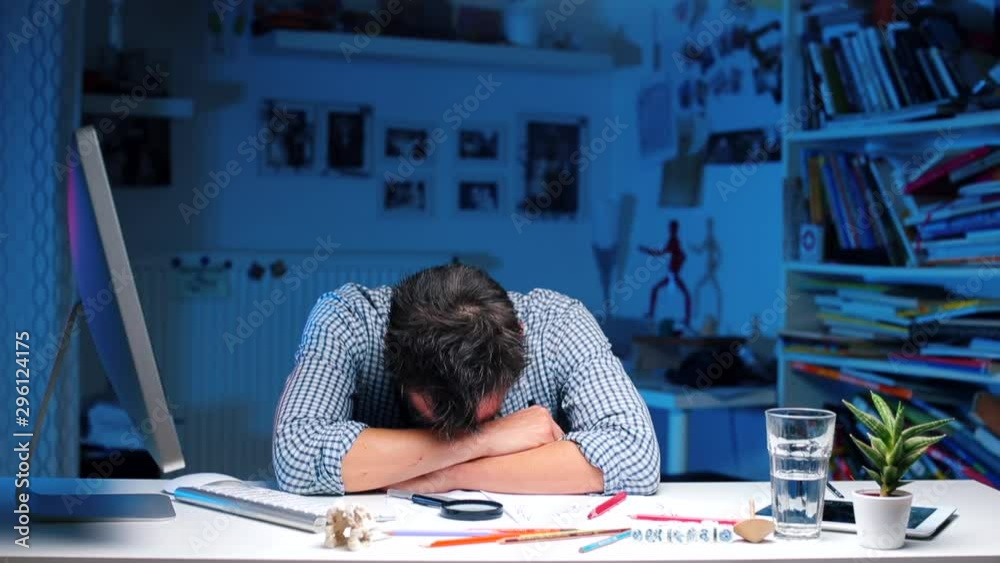 A man sleeps on a table in an office. He is thrown documents on the table.