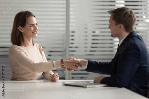 Confident businessman shaking hand of smiling businesswoman in office