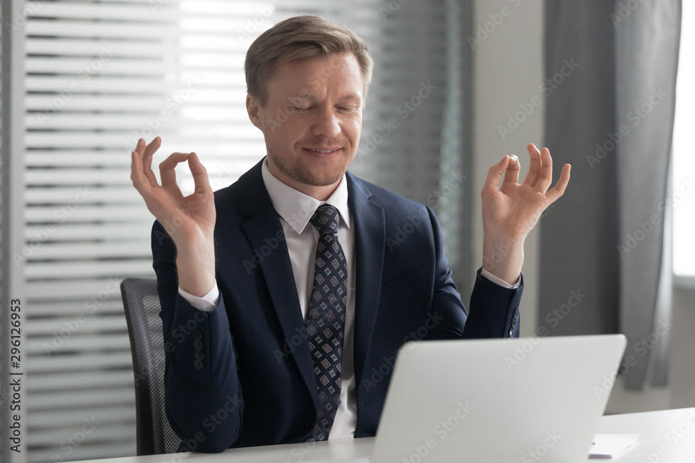 Satisfied businessman relaxing, meditating in yoga pose at workplace Satisfied businessman relaxing, meditating in yoga pose at workplace