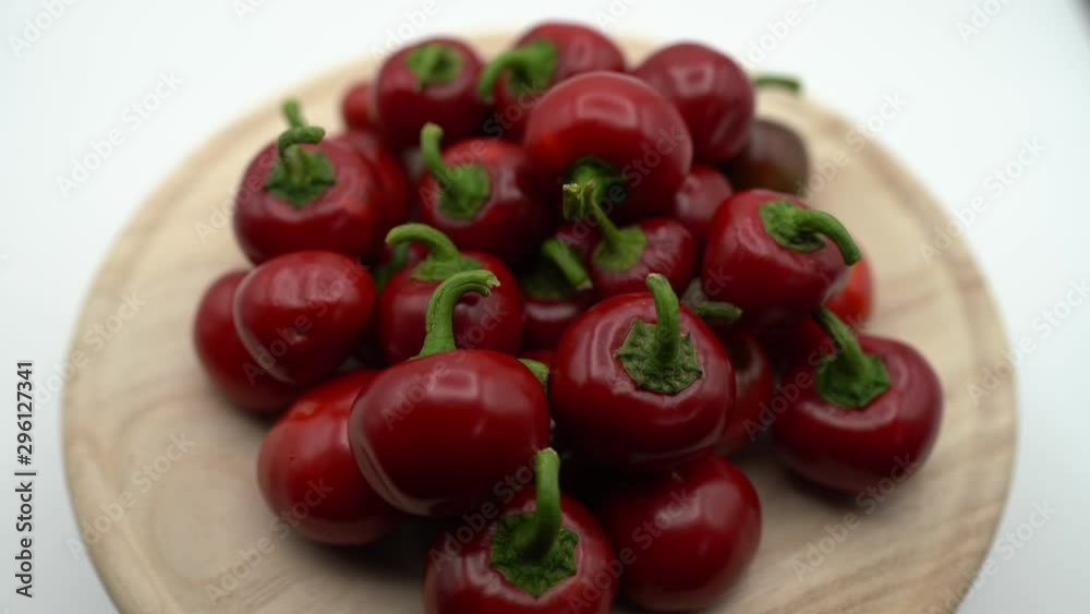 Fresh red hot chili peppers rotating on white background on wooden plate. Small round raw hot peppers fiery. Close-up of hot chili peppers ready for eating. Vegeterian healthy nutrition concept Fresh red hot chili peppers rotating on white background on wooden plate. Small round raw hot peppers fiery. Close-up of hot chili peppers ready for eating. Vegeterian healthy nutrition concept