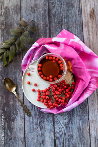 Hot healing tea, mountain ash tea. Reduces the level of harmful cholesterol in the blood, strengthens blood vessels. healing drink on a wooden background with a pink napkin
