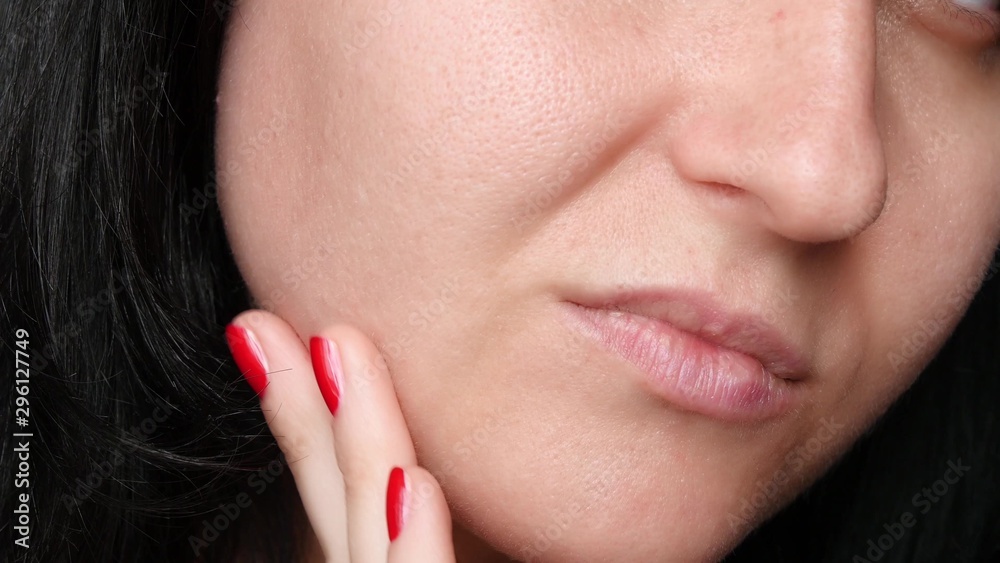 Obraz premium Female face close-up. Skin texture with enlarged pores. The girl touches the fingers of the problem skin of the face, considering it. The concept of care for problem skin, age-related changes and the