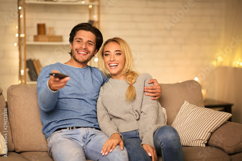 Happy spouses watching TV on sofa in the evening