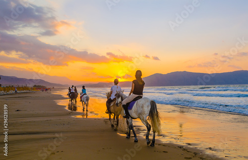 A group of girls on horseback riding on a sandy beach on the background of the sunset sky