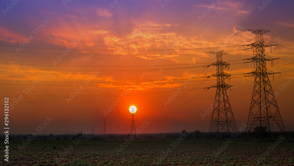 Obraz premium high voltage post and high voltage tower electric transmission tower system with blue sky sunset silhouette with blue sky sunset, white clouds and meadow and grass in the evening.