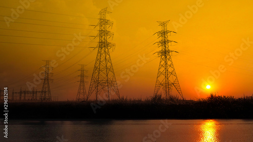 high voltage post or high voltage tower electric transmission tower system with gloden sky sunset silhouette near pond in the evening,landscaping shot photo.