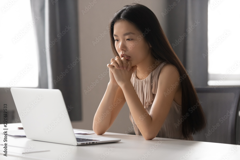 Thoughtful Asian businesswoman looking at laptop screen, pondering task Thoughtful Asian businesswoman looking at laptop screen, pondering task