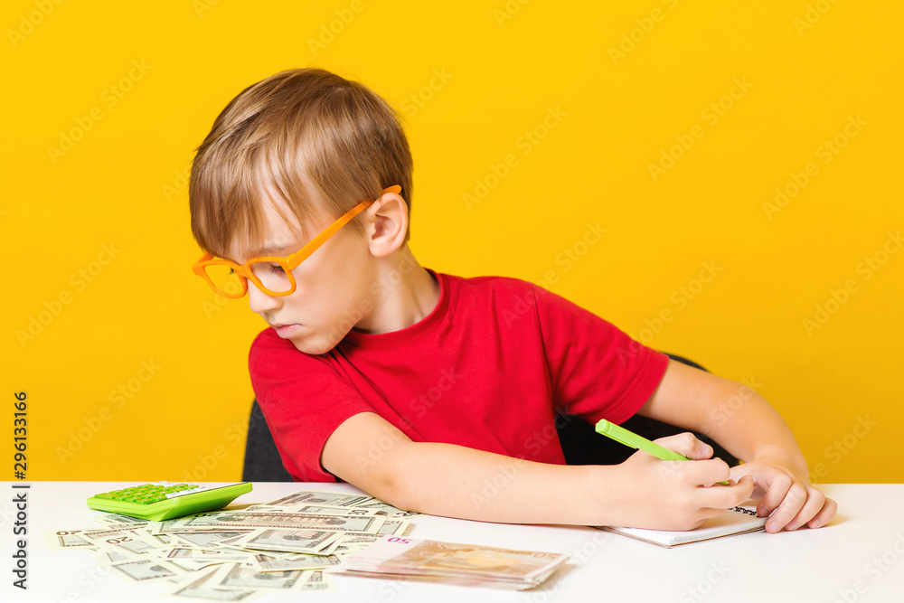 Little boy saving money for future education. Learning financial responsibility and projecting savings. Kid at table counts money Little boy saving money for future education. Learning financial responsibility and projecting savings. Kid at table counts money