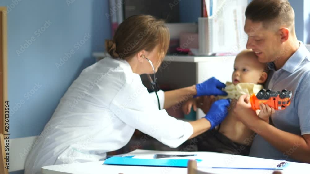 Female doctor examines a small one and a half year old boy. Father and his baby at a pediatrician's appointment. Father's day Female doctor examines a small one and a half year old boy. Father and his baby at a pediatrician's appointment. Father's day