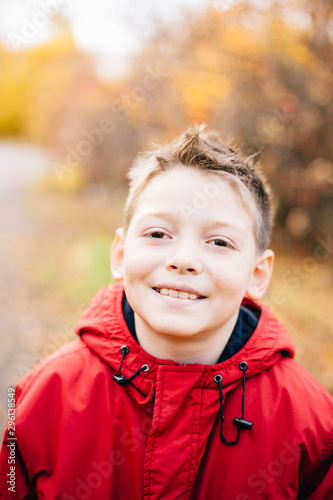 Portrait of smiling boy looking at camera, wearing red jacket, isolated on autumn background