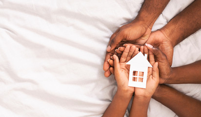 Black family of three holding paper house figure in hands