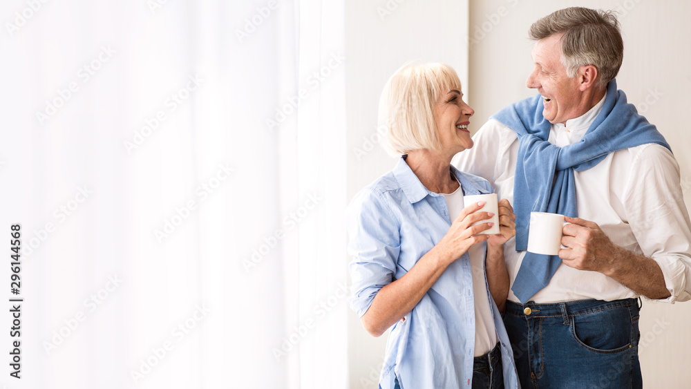 Happy senior couple talking near window and drinking tea