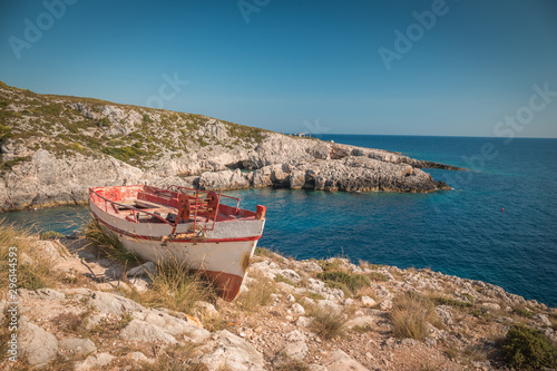 The old abandoned wooden fishing boat on a rocky cliff shore on a sunny day in greece. Zakynthos. Blue sea in the background.