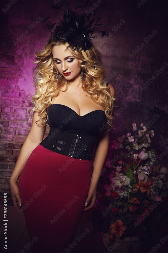 Art fashion portrait of a young beautiful elegant blonde woman with massive sparkling earrings,fashion black hat with feathers,makeup and hairstyle posing in corset and long tight pink skirt 