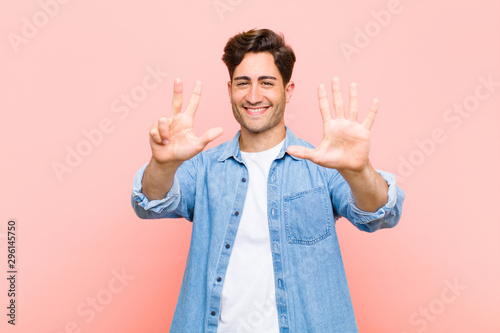 young handsome man smiling and looking friendly, showing number eight or eighth with hand forward, counting down against pink background photo