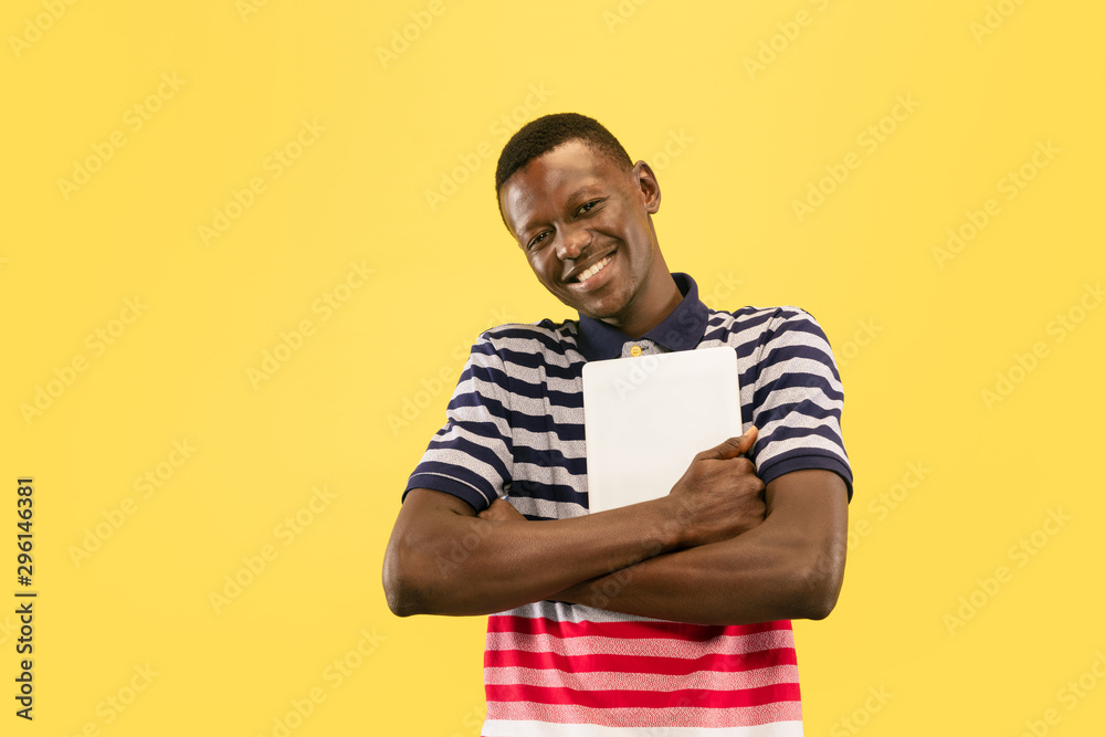 Happy young african-american man with tablet isolated on yellow studio background, facial expression. Beautiful male half-lenght portrait. Concept of human emotions, facial expression.
