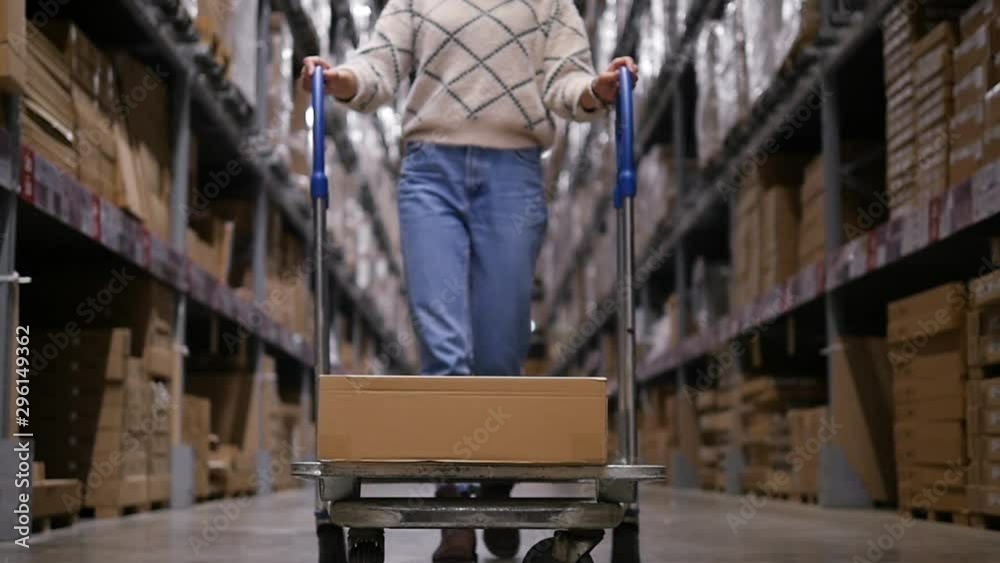 Beautiful modern woman is carrying a trolley with a box. Close-up of a cart with a box in motion Beautiful modern woman is carrying a trolley with a box. Close-up of a cart with a box in motion