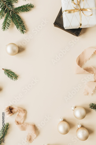 Christmas / New Year holiday composition. Mock up frame with blank copy space made of fir needle branches, gift boxes, ribbons and Christmas baubles on beige background. Flat lay, top view.