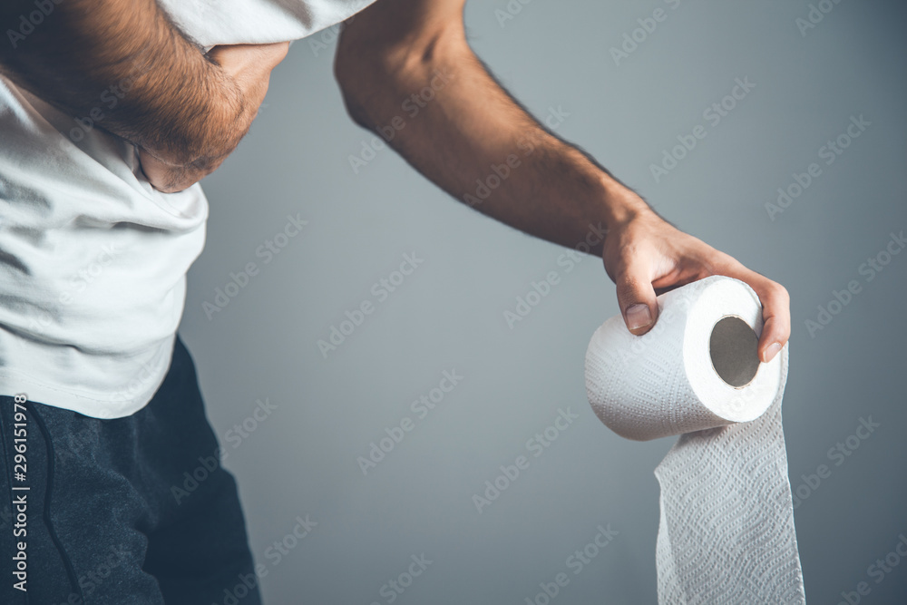 Fototapeta premium man holding a roll of toilet paper on gray background