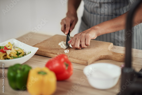 Close up of mixed race woman in apron standing in kitchen and chopping mushrooms.