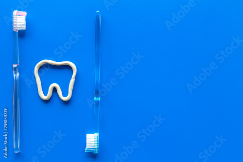 Teeth brushing concept. Tooth drawn with toothpaste near toothbrushes on blue background top view copy space