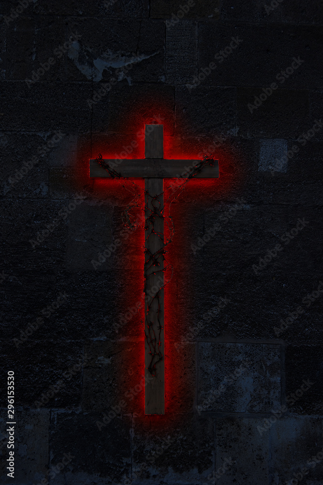 Big ominous wooden crucifix on a dark, stone wall wrapped in incandescent barbed wire with red glow underneath 