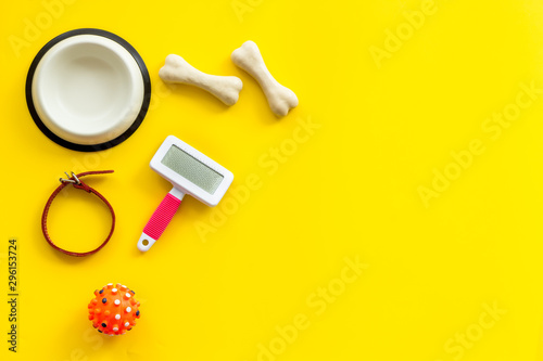 Set of treats and toys for pets with bones, collar and bowl on yellow background top view frame space for text
