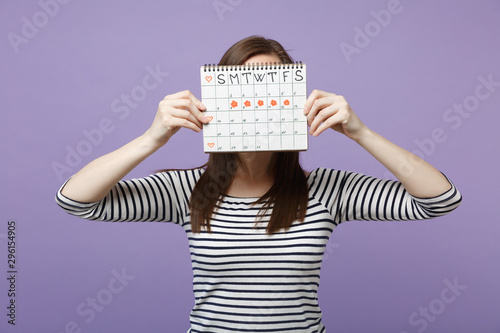 Woman hold cover face hiding female periods calendar for checking menstruation days isolated on violet purple background studio portrait. Medical healthcare gynecological concept. Mock up copy space. photo