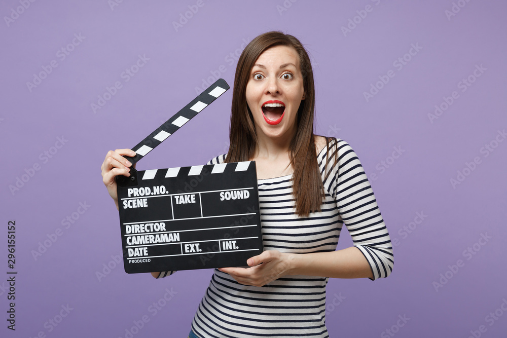 Young fun woman girl in casual striped clothes posing isolated on violet purple background studio portrait. People sincere emotions lifestyle concept. Mock up copy space. Hold film making clapperboard