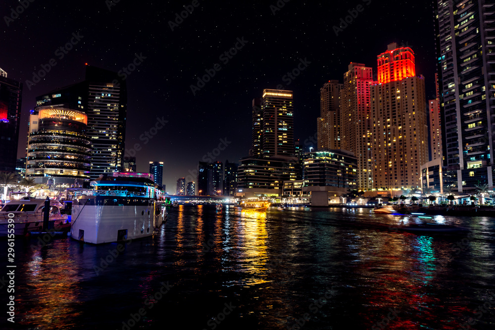 Fototapeta premium Dubai Marina at night with light reflections on the water, starry sky and a dhow cruise