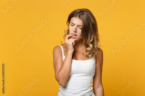 Preoccupied nervous young woman girl in light casual clothes posing isolated on yellow orange background, studio portrait. People sincere emotions lifestyle concept. Mock up copy space. Gnawing nails.