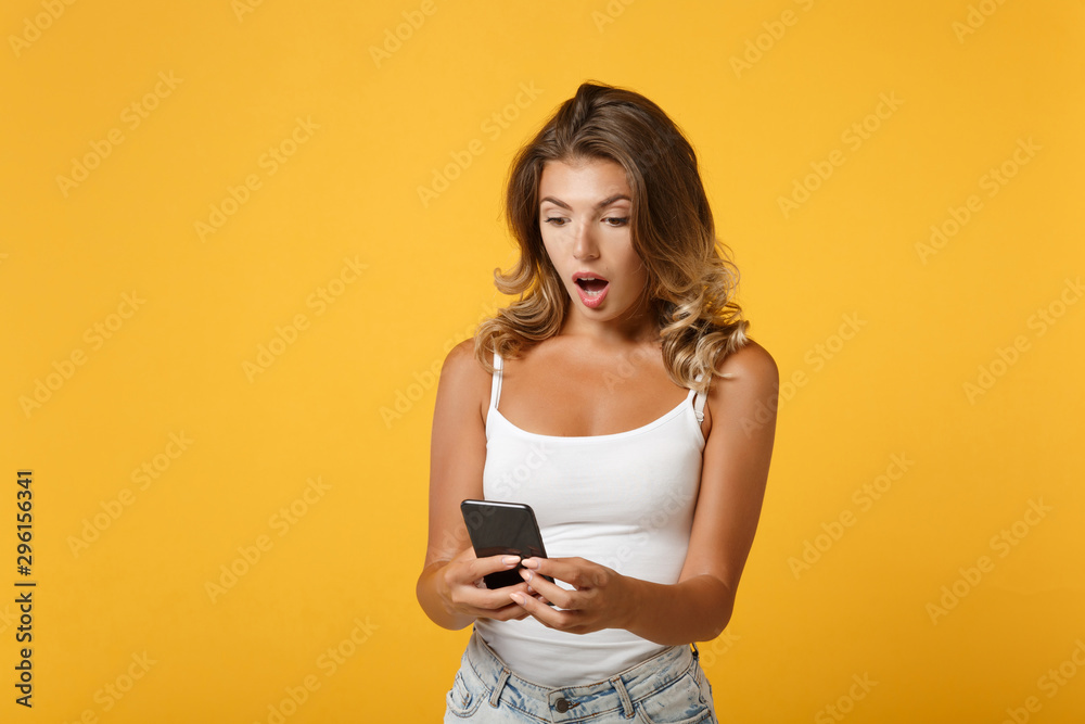 Shocked young woman girl in light casual clothes posing isolated on yellow orange wall background studio portrait. People lifestyle concept. Mock up copy space. Using mobile phone, typing sms message. Shocked young woman girl in light casual clothes posing isolated on yellow orange wall background studio portrait. People lifestyle concept. Mock up copy space. Using mobile phone, typing sms message.