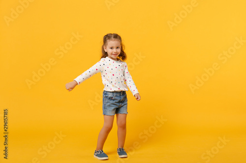Little cute child kid baby girl 4-5 years old wearing light denim clothes isolated on pastel yellow wall background, children studio portrait. Mother's Day, love family, parenthood childhood concept.
