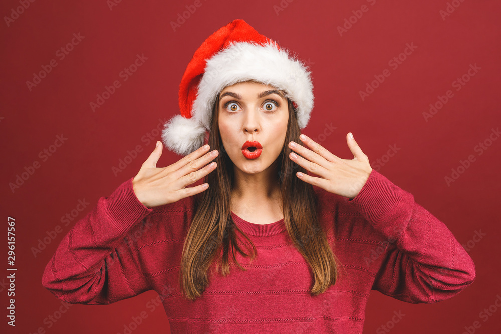 Attractive Woman With Santa Hat Looking Surprised And Amazed isolated against red background. Attractive Woman With Santa Hat Looking Surprised And Amazed isolated against red background.
