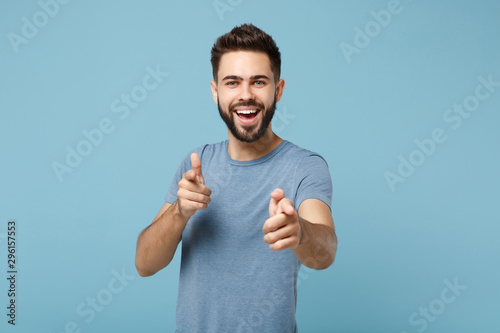 Young cheerful handsome man in casual clothes posing isolated on blue wall background, studio portrait. People sincere emotions lifestyle concept. Mock up copy space. Pointing index fingers on camera.