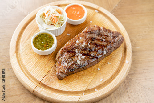 Grilled striploin steak with Pickled cabbage and two sauces. The strip steak, also called a New York strip. Serving on a wooden Board. Barbecue restaurant menu, a series of photos of different meats.