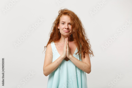 Young pleading redhead woman in casual light clothes posing isolated on white background  studio portrait. People sincere emotions lifestyle concept. Mock up copy space. Holding hands folded in pray.