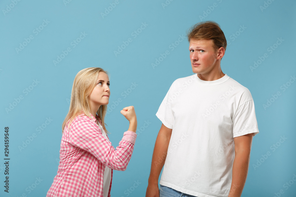Young couple two friends guy girl in white pink empty blank design t-shirts posing isolated on pastel blue background in studio. People lifestyle concept. Mock up copy space. Swearing, clenching fist. Young couple two friends guy girl in white pink empty blank design t-shirts posing isolated on pastel blue background in studio. People lifestyle concept. Mock up copy space. Swearing, clenching fist.