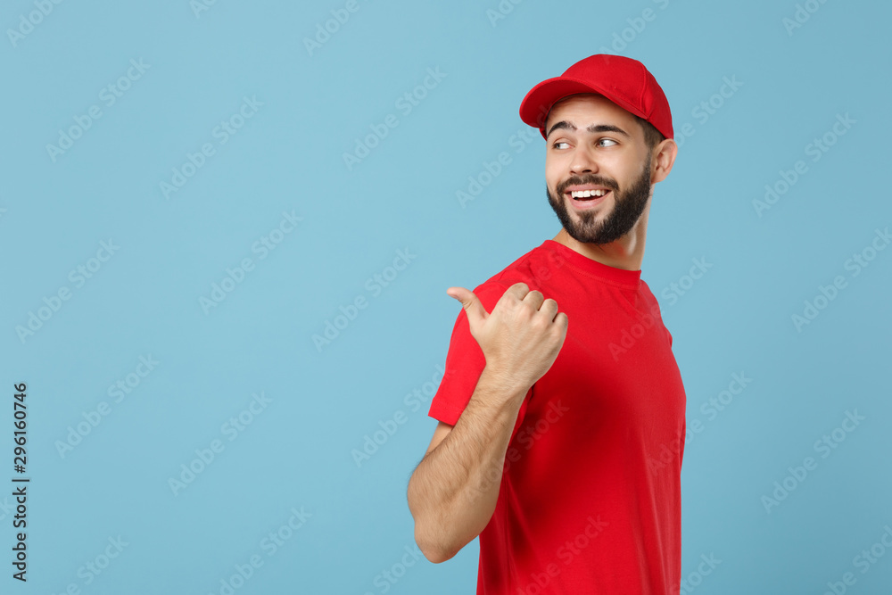 Delivery man in red uniform workwear isolated on blue wall background, studio portrait. Professional male employee in cap t-shirt print working as courier dealer. Service concept. Mock up copy space. Delivery man in red uniform workwear isolated on blue wall background, studio portrait. Professional male employee in cap t-shirt print working as courier dealer. Service concept. Mock up copy space.
