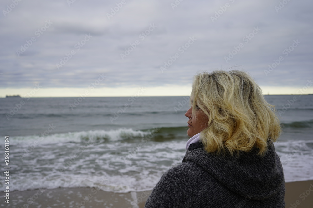 A girl looks into the distance against the backdrop of a cold sea. Blond hair in the wind. Hair and sea breeze. close-up. A girl looks into the distance against the backdrop of a cold sea. Blond hair in the wind. Hair and sea breeze. close-up.