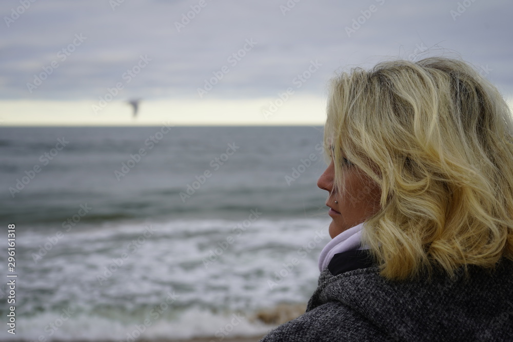 A girl looks into the distance against the backdrop of a cold sea. Blond hair in the wind. Hair and sea breeze. close-up.